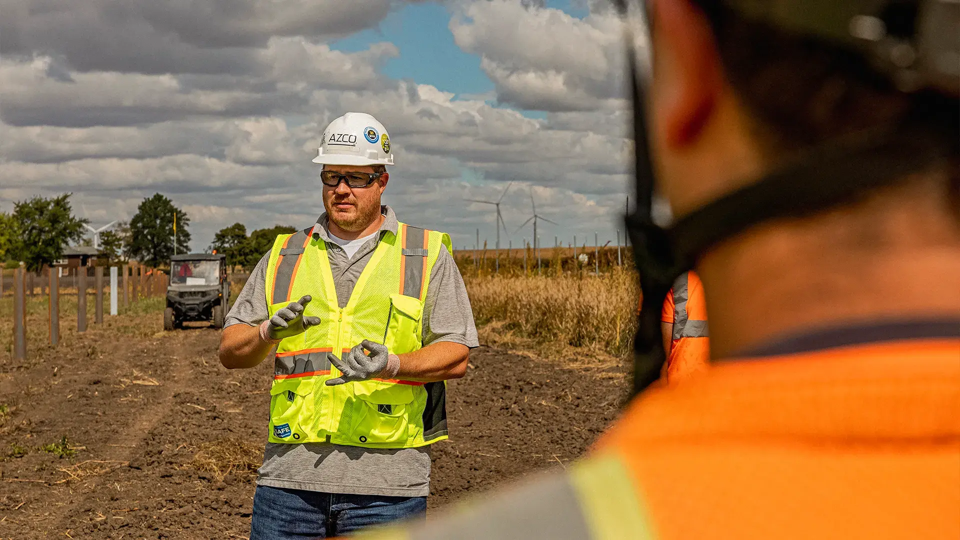 Two men engage in conversation, one wearing a safety vest for visibility.